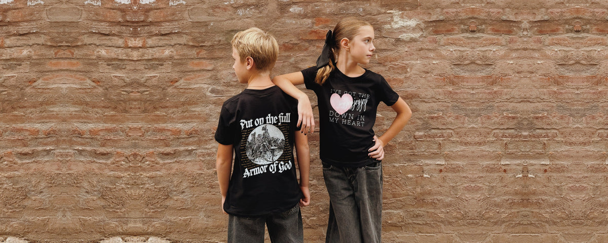 Armor of God and Joy Joy Joy youth tees against a brick wall