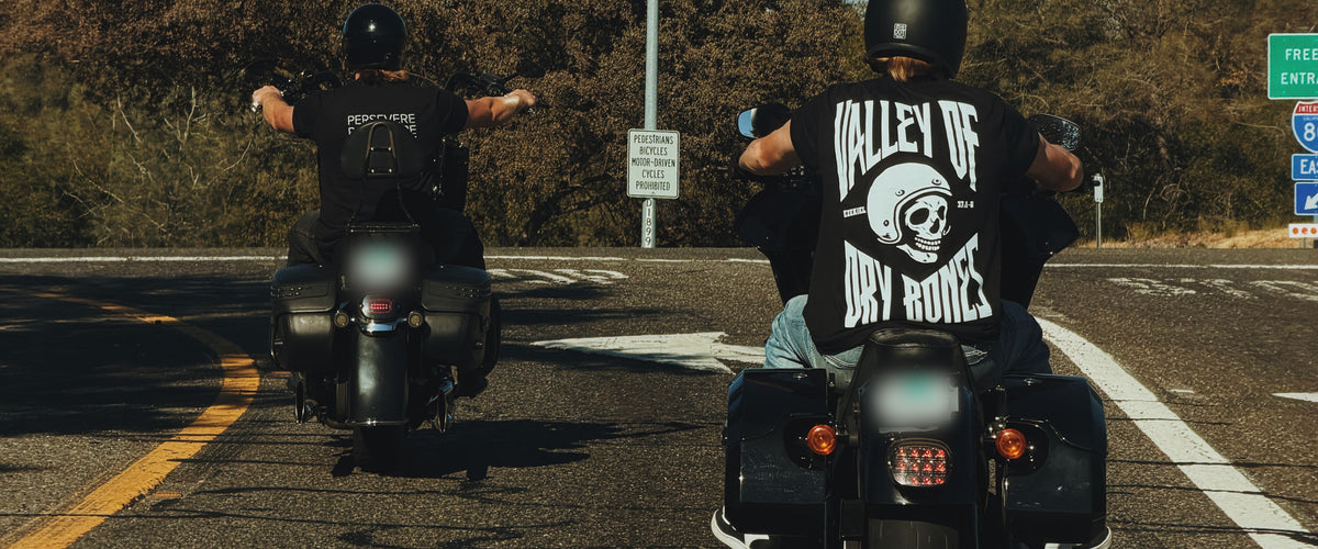 Two riders in Bee and Lion tees pulling away on motorcycles