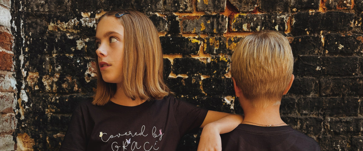 Two kids in Bee and Lion tees against a brick wall